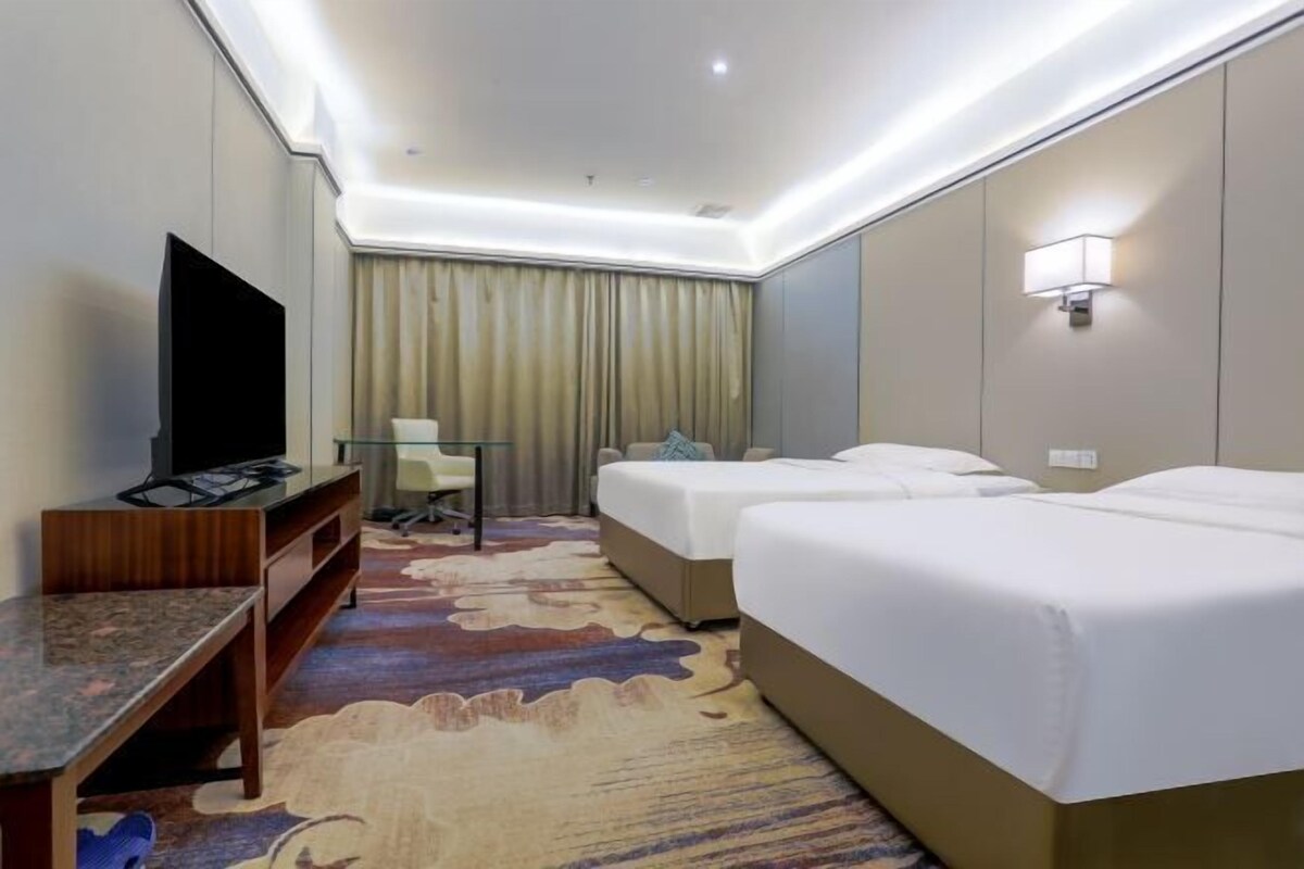 A hotel room with two beds, a TV, a desk, a chair, and a large patterned rug.