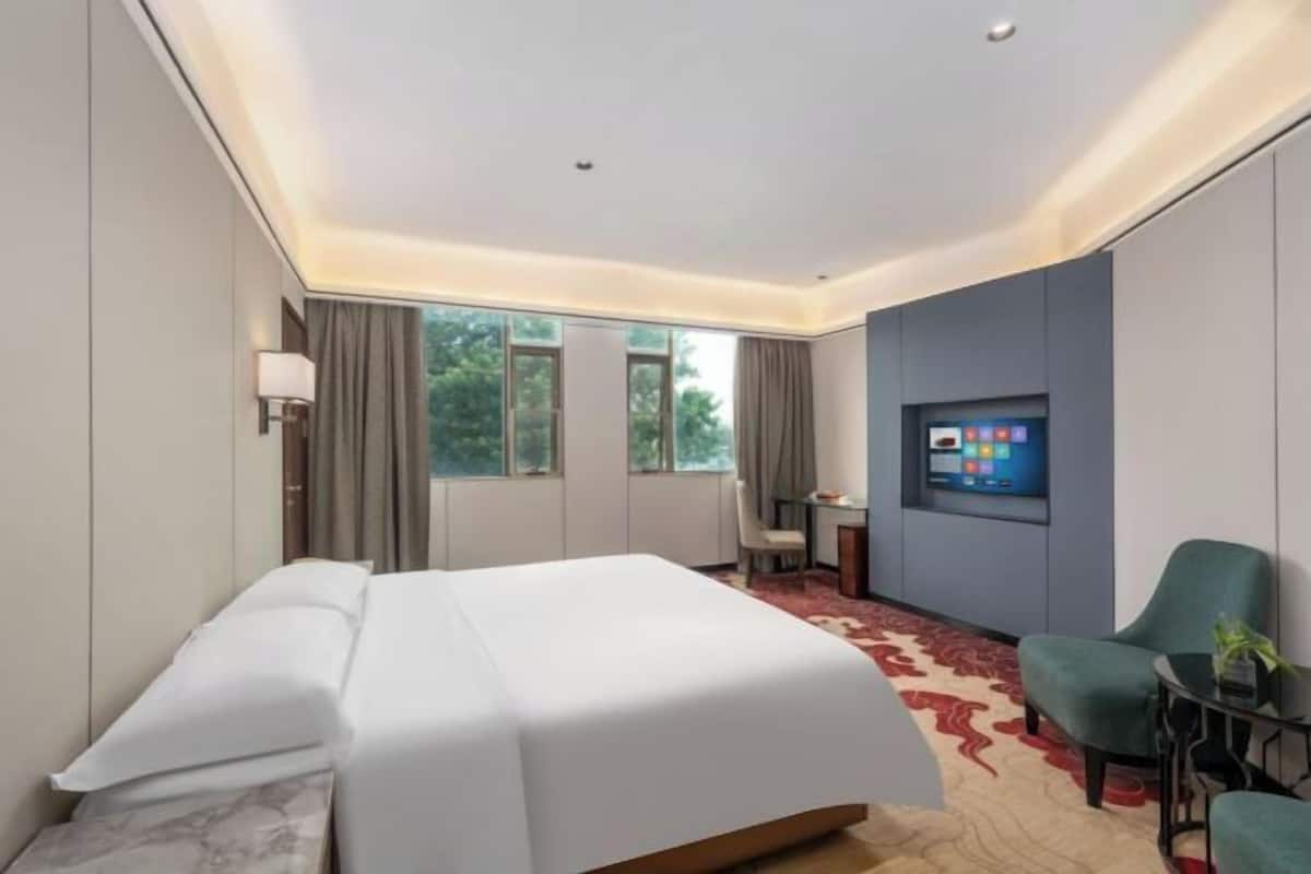Ein Hotelzimmer mit Bett, Schreibtisch, Sessel, Fernseher und Fenster.