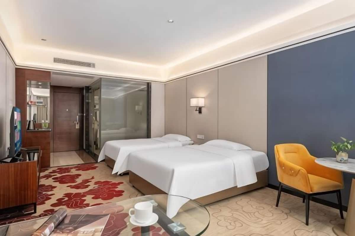 Ein Hotelzimmer mit zwei Betten, einem kleinen Tisch, einem Stuhl, einem Schreibtisch und einem Spiegel.