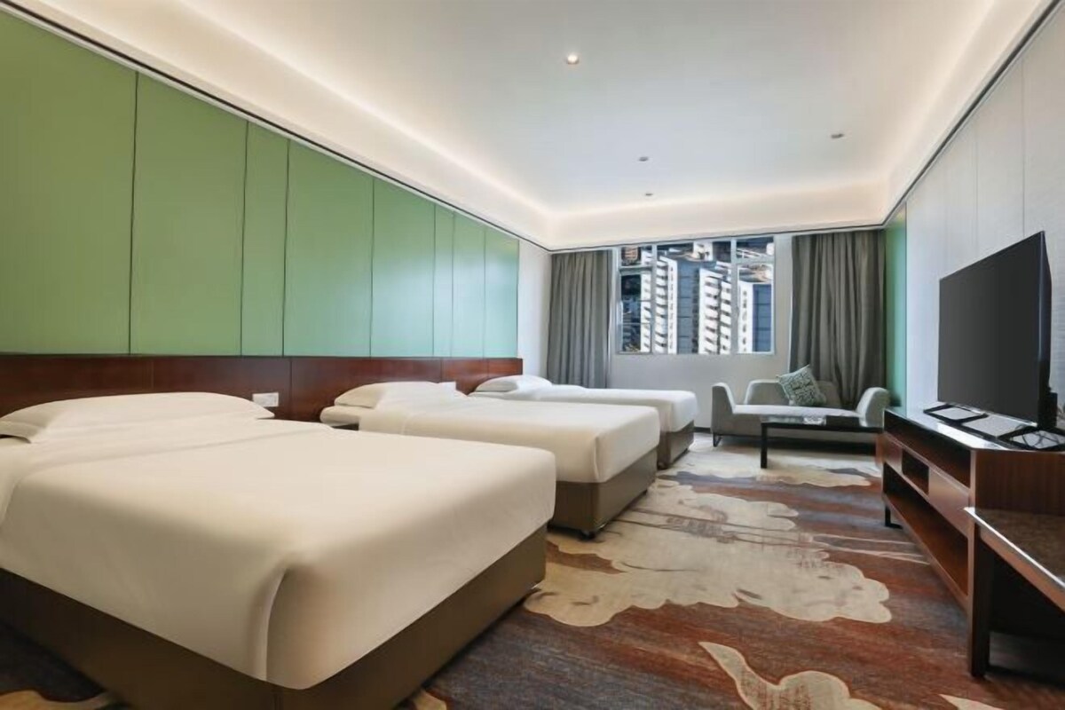 A hotel room with two beds, a sofa, a TV, and a view of buildings.