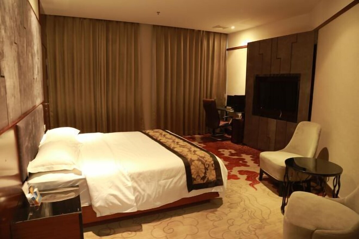 A hotel room with a bed, a desk, a chair, a TV, and a large window with curtains.