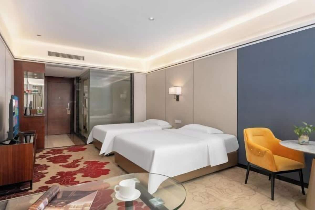 Ein Hotelzimmer mit zwei Betten, einem Schreibtisch mit Stuhl, einem kleinen Tisch mit Tasse und einem dekorativen Teppich.