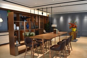 A modern hotel lobby with a wooden reception desk, bar stools, and a seating area with a table and chairs.