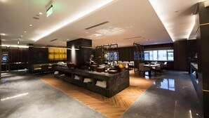 Un moderno vestíbulo de hotel con una zona de bar central, espacios de descanso y un amplio ventanal que proporciona luz natural.