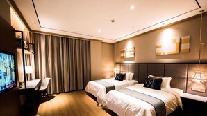 Habitación de hotel con dos camas, un escritorio, televisor y un amplio ventanal con cortinas.