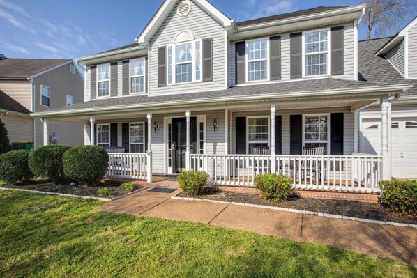 Stunning two-story home with a central entrance, white porch, and neatly manicured front yard.