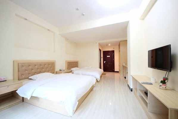 Une chambre d’hôtel avec deux lits, une télévision, un bureau et une porte donnant sur une autre chambre.