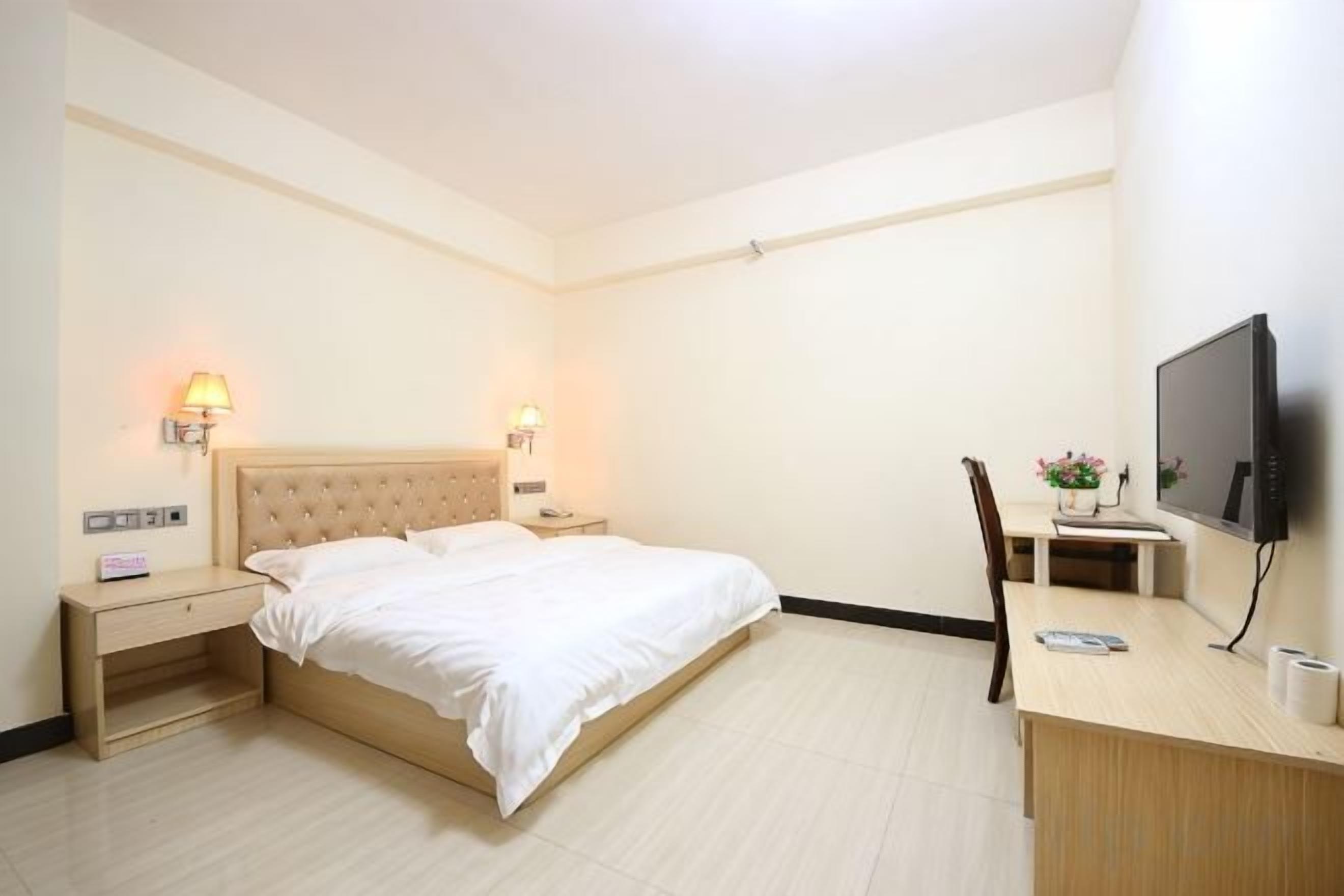 Habitación de hotel con cama, mesitas de noche, escritorio con silla, televisor y televisor montado en la pared.