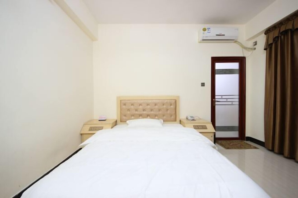 A hotel room with a bed, a nightstand, an air conditioning unit, and a door leading to a balcony.