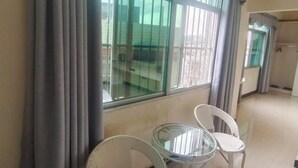 Ein Zimmer mit Balkon, einem Glastisch und zwei Korbstühlen.
