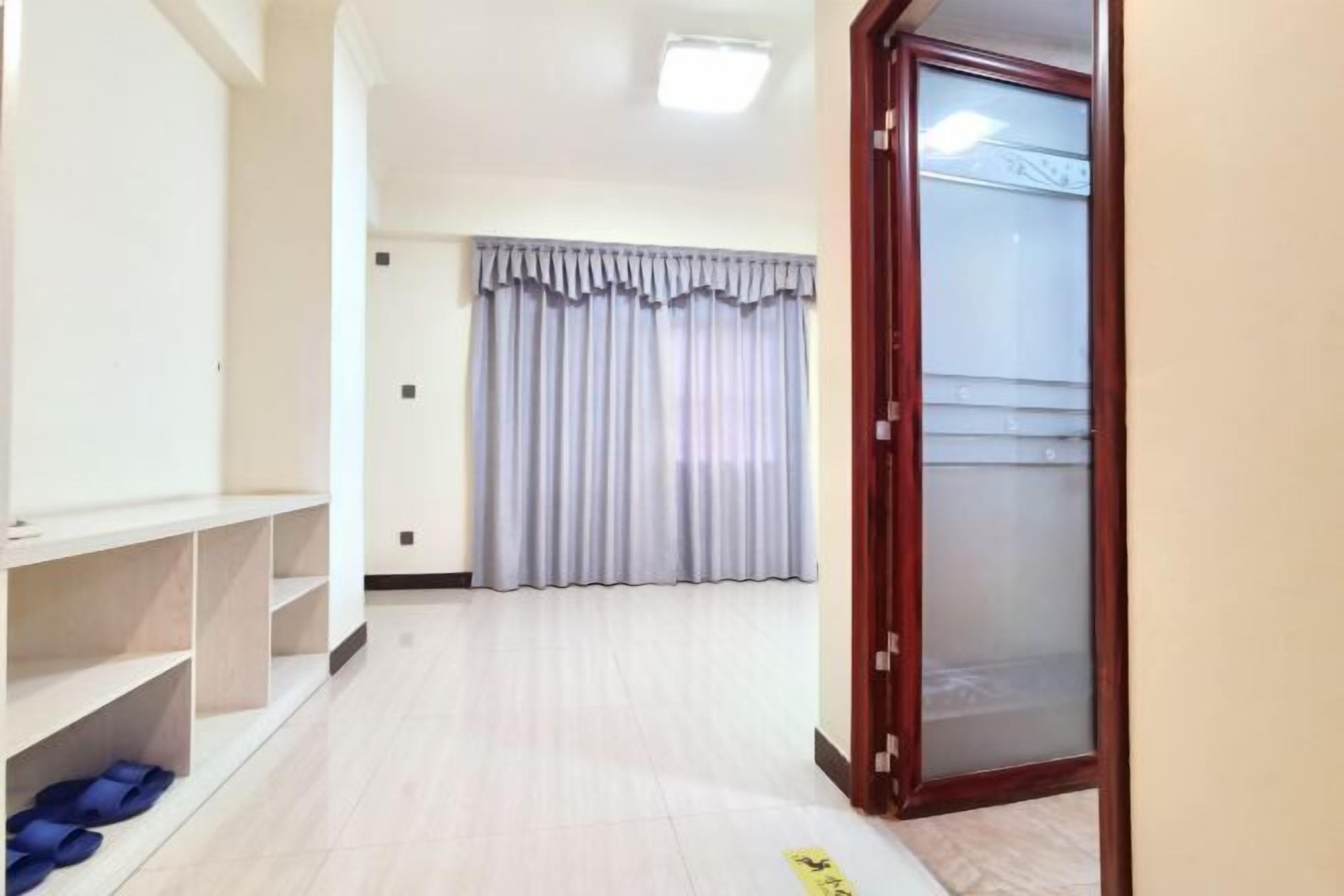 A hallway with a wooden floor, a set of shelves, a pair of blue slippers, and a frosted glass door.