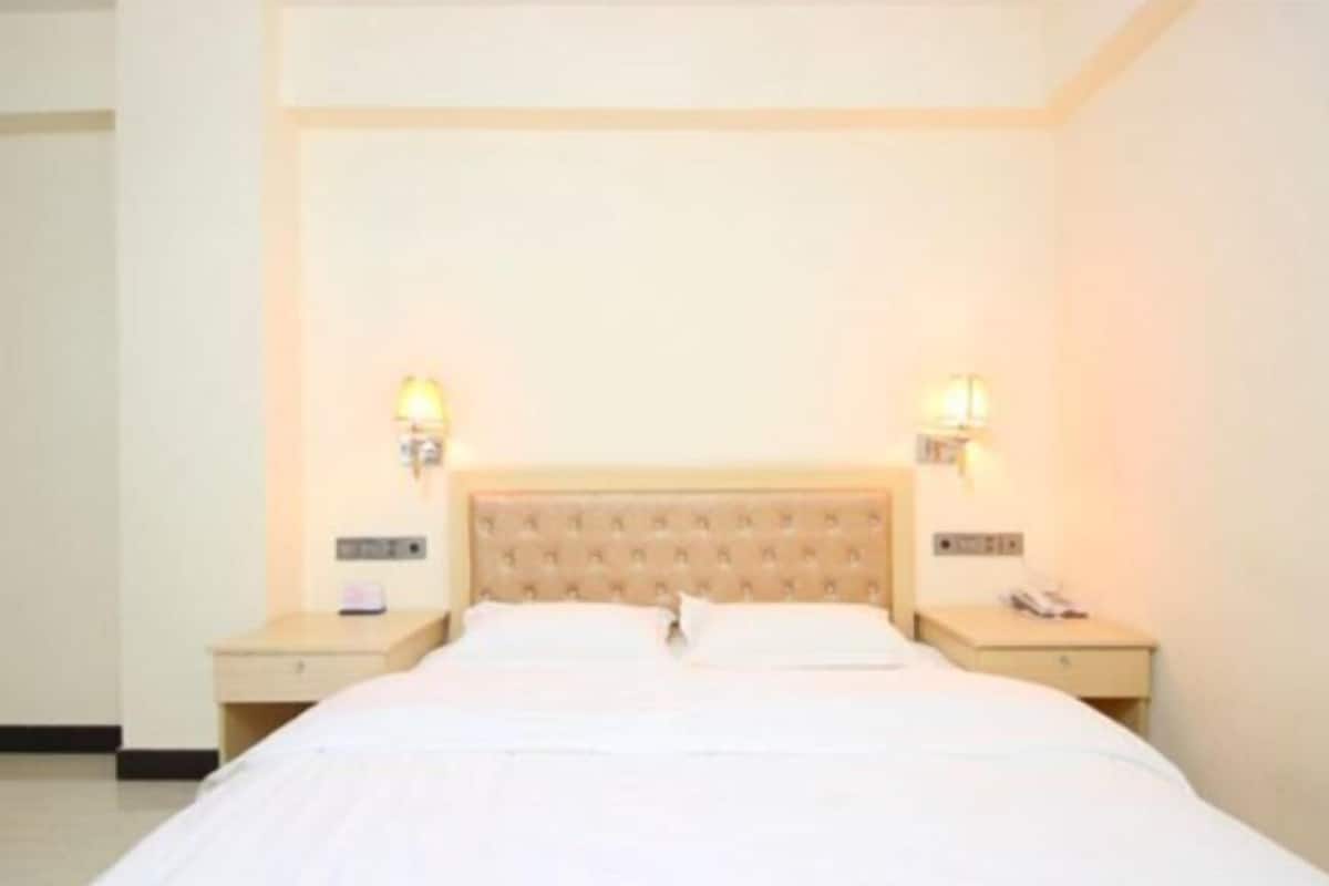 Une chambre d’hôtel avec un grand lit, deux tables de chevet et des lampes fixées au mur.