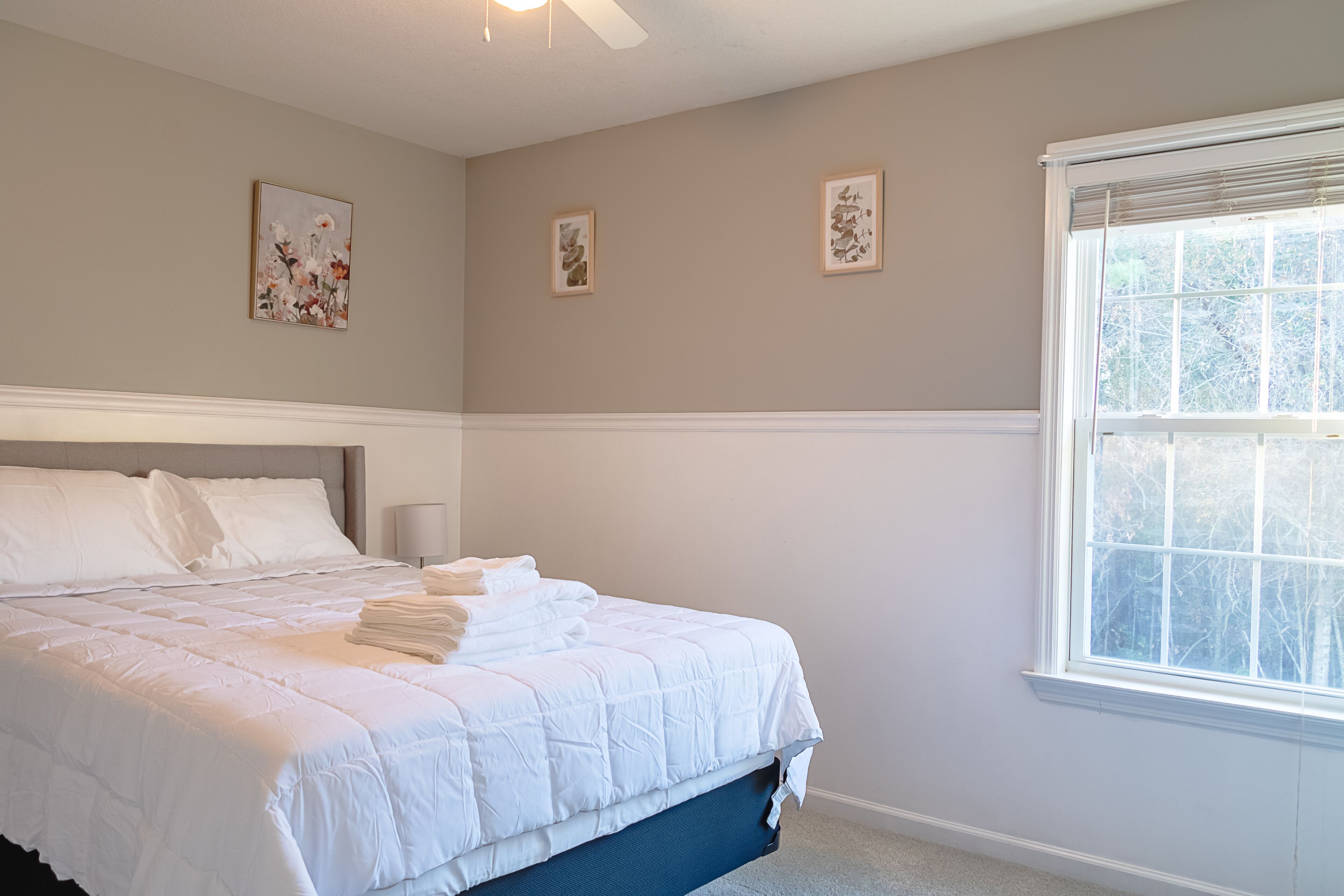 A bedroom with a large bed, a window with blinds, and three framed pictures on the wall.