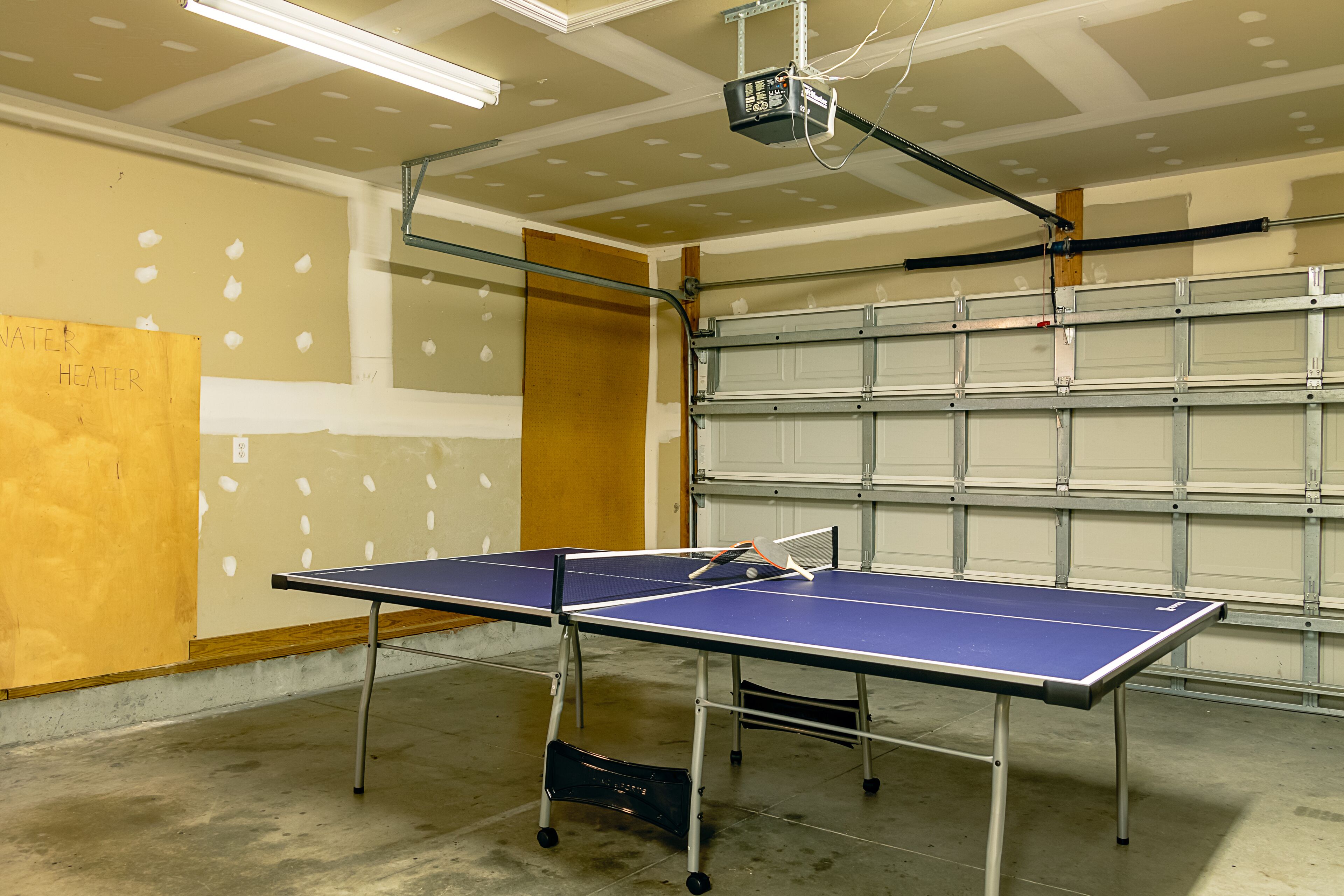 A ping pong table in a room with unfinished walls and a garage door.