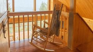 Une cabane en bois avec un plafond en pente, un fauteuil à bascule et une vue sur l’extérieur.