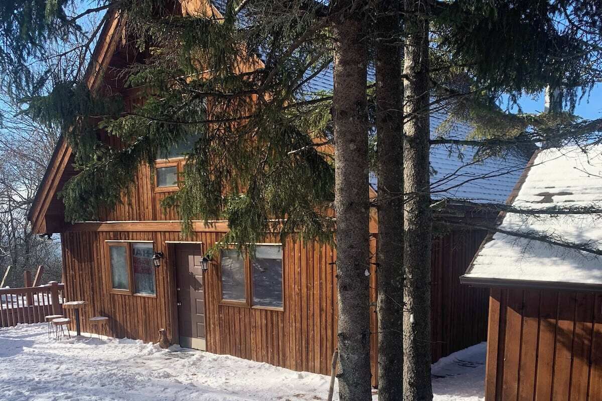 Lumihunnun peittämä puinen mökki, jonka ympärillä on puita.