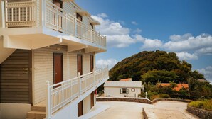 A hotel with a balcony, a view of a hill, and a clear sky.
