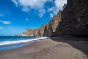 Una playa con un acantilado rocoso y cielo azul despejado.