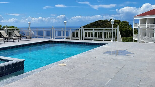 A rectangular swimming pool with a white tiled deck, surrounded by white railings and lounge chairs.
