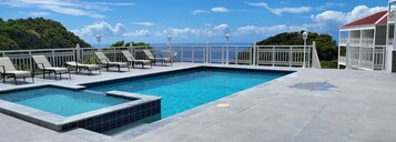 Una piscina rectangular con borde de azulejos blancos, rodeada de barandillas y sillas de descanso blancas.
