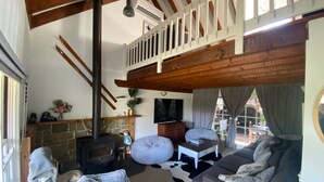 Un salon chaleureux avec une cheminée en pierre, un canapé, un téléviseur et un balcon doté d’une balustrade en bois.