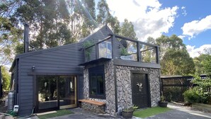 Une maison moderne avec une façade en pierre, une grande porte vitrée et un banc en bois à l’extérieur.