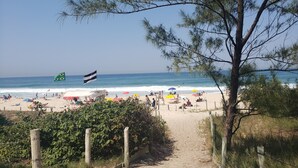 Une plage avec un sentier de sable menant au bord de l’eau, des parasols et un drapeau.
