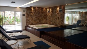 Un espace spa agrémenté d’un mur en pierre, d’un bain à remous et de chaises longues.