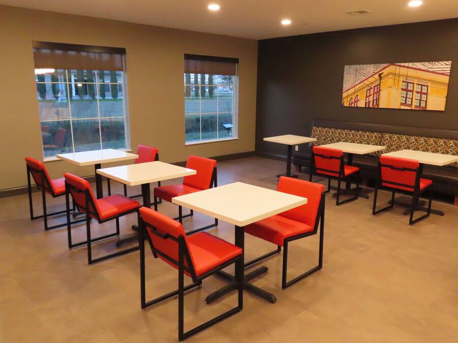 A restaurant with tables and chairs, large windows, and a wall with a painting.