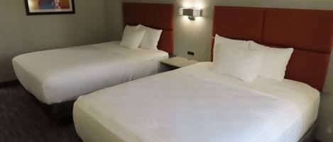 Two single beds with white linens, a nightstand, a wall-mounted light, and a framed picture on the wall.