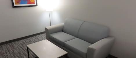 A room with a grey sofa, a white table, and a framed abstract painting on the wall.