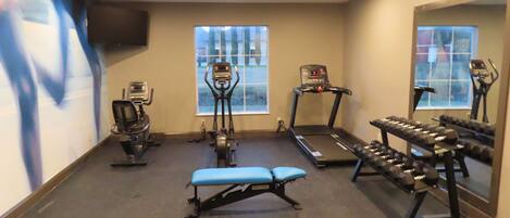 A gym with cardio machines, weight benches, and dumbbells.