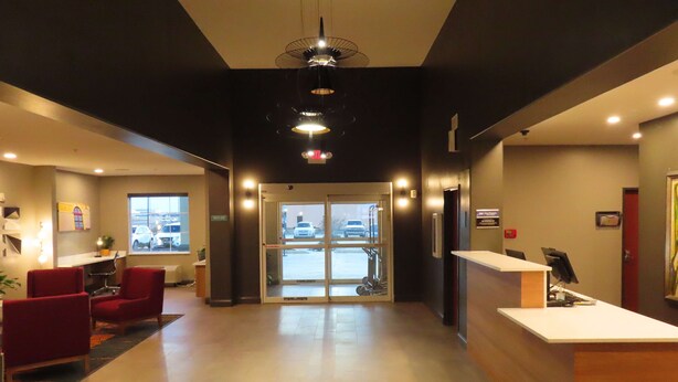 A hotel lobby with a reception desk, red chairs, a large window, and a view of parked cars outside.