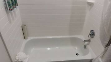 A white-tiled bathroom with a bathtub, a towel, and a soap dispenser.