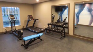 A gym with cardio machines, dumbbells, and a bench.
