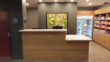 A reception desk with a check-in counter, a refrigerator stocked with beverages, and a snack vending machine.