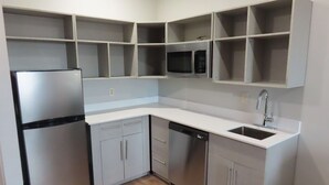 A modern kitchen with a stainless steel refrigerator, dishwasher, and microwave. It includes white cabinetry and a white countertop.