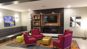 A modern living room with a black marble fireplace, red and yellow chairs, a flat-screen TV, and a colorful abstract painting.