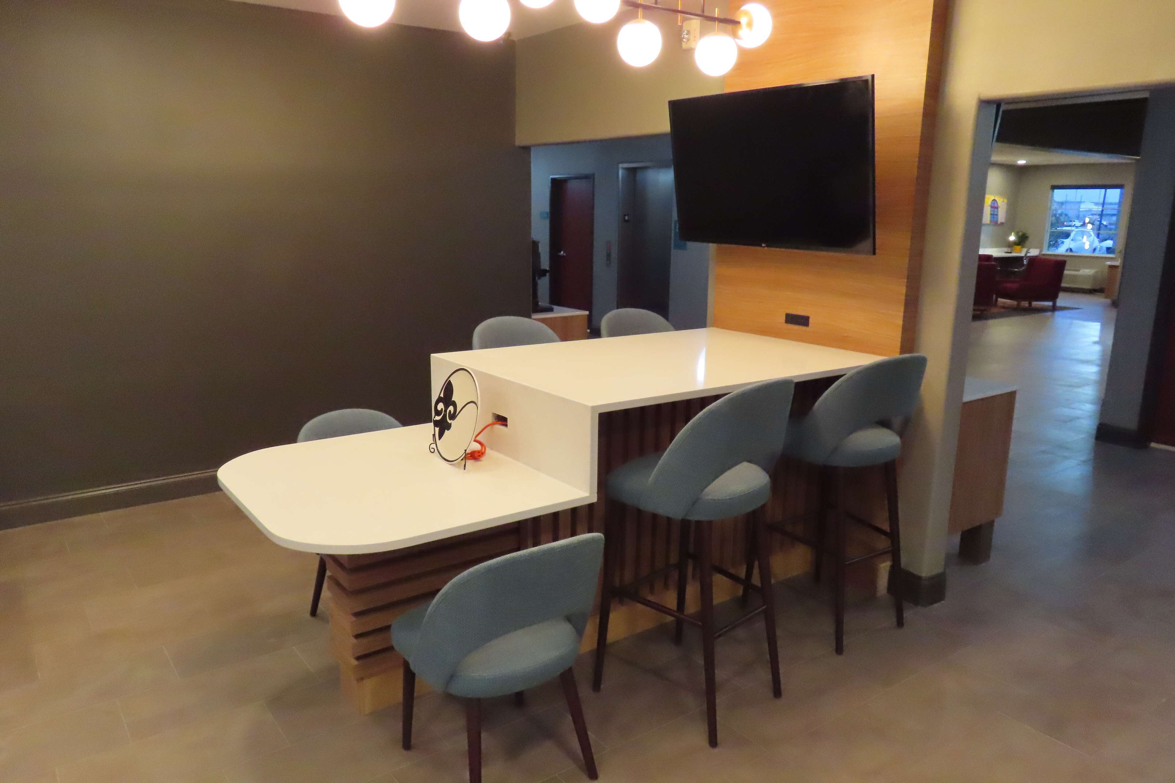 A modern conference room with a white table, six blue chairs, a flat-screen TV mounted on the wall, and a wooden accent wall.