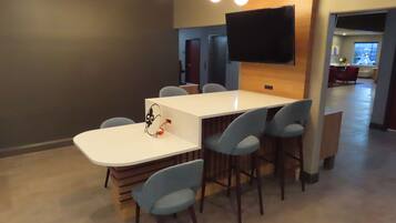 A modern conference room with a white table, six blue chairs, a flat-screen TV mounted on the wall, and a wooden accent wall.