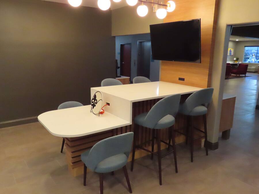 Un salón de conferencias moderno con una mesa blanca, seis sillas azules, un televisor de pantalla plana montado en la pared y una pared de acento de madera.
