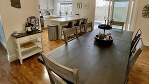 A spacious dining area with a large table and chairs, a kitchen in the background, and a view through a sliding glass door. - Cactus Oasis -Cheerful 3 bedroom family home with heated pool. (Phoenix)