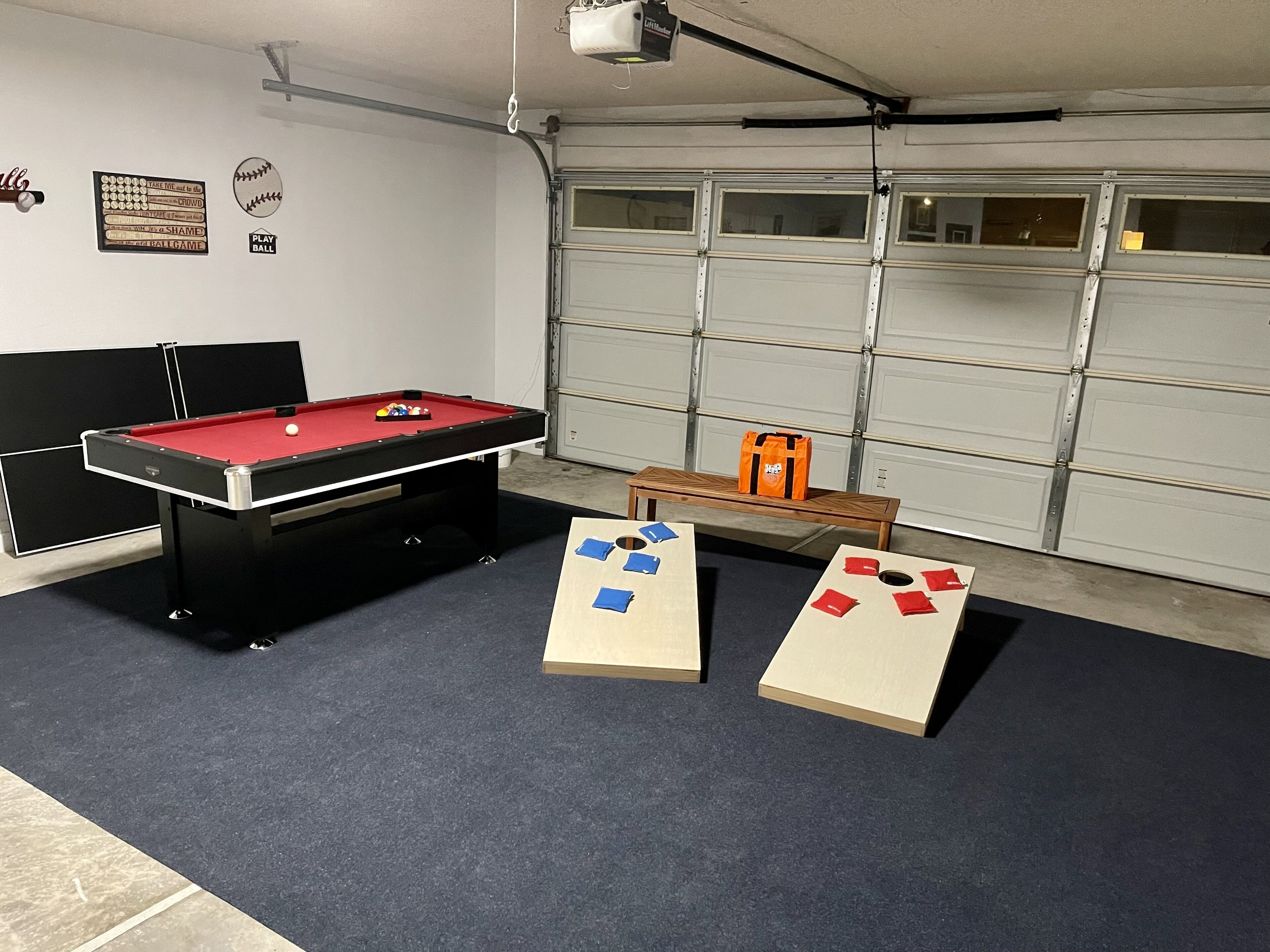 Een pooltafel met een rode viltbekleding, een tafeltje met een tas, en twee tafelvoetbaltafels met schijven.
