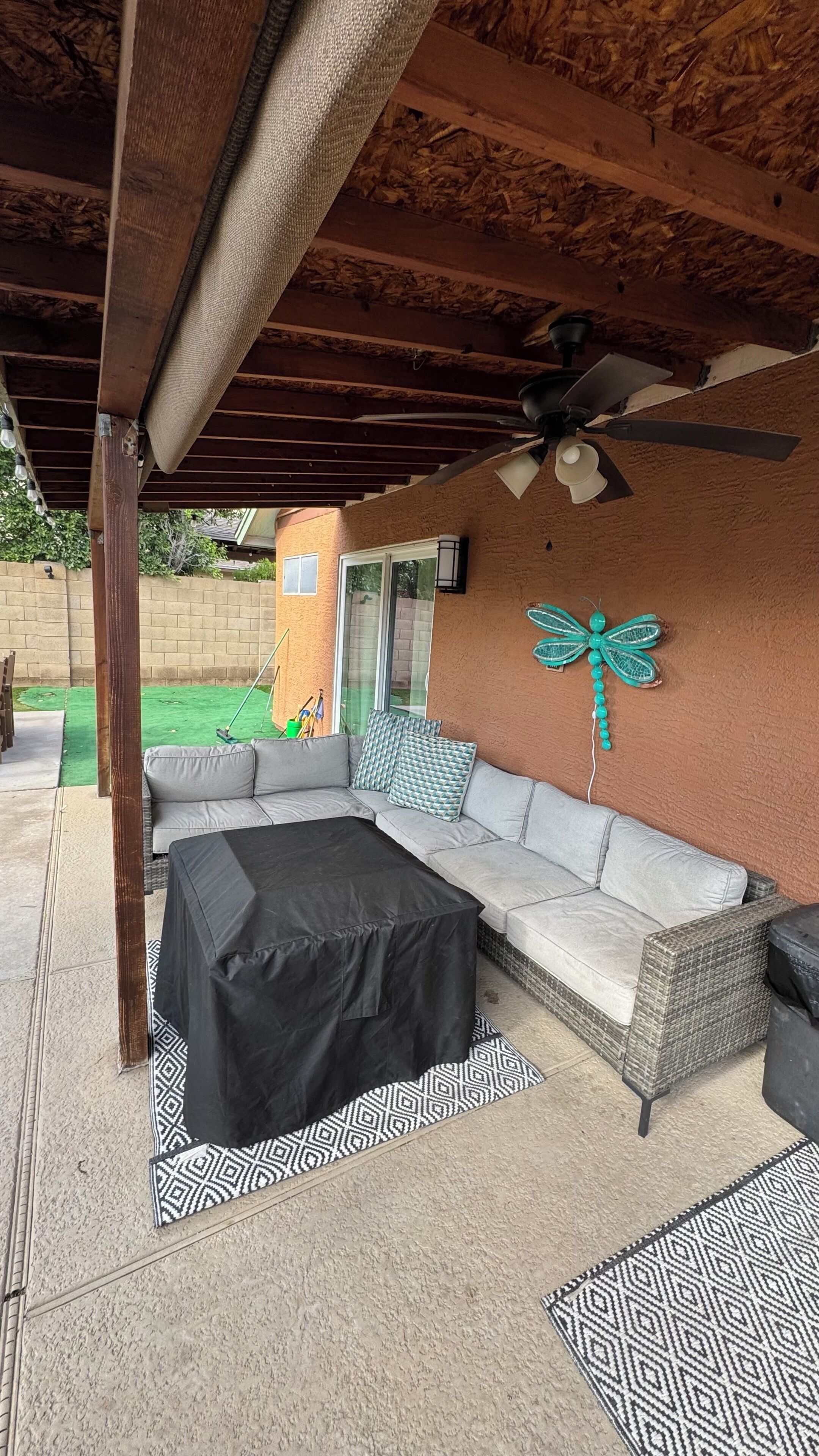 A covered patio area with a sofa, a black table, patterned rugs, and a ceiling fan.