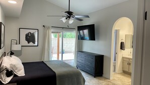 A bedroom with a bed, a ceiling fan, a TV, a dresser, and a bathroom visible through an archway. - Cactus Oasis -Cheerful 3 bedroom family home with heated pool. (Phoenix)