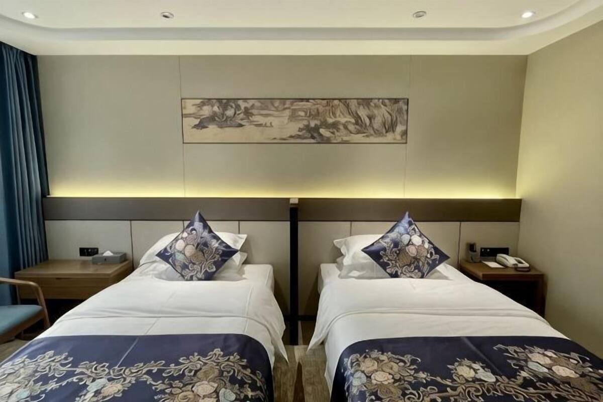 A hotel room with two beds, a desk, a chair, a nightstand, and a wall-mounted artwork.