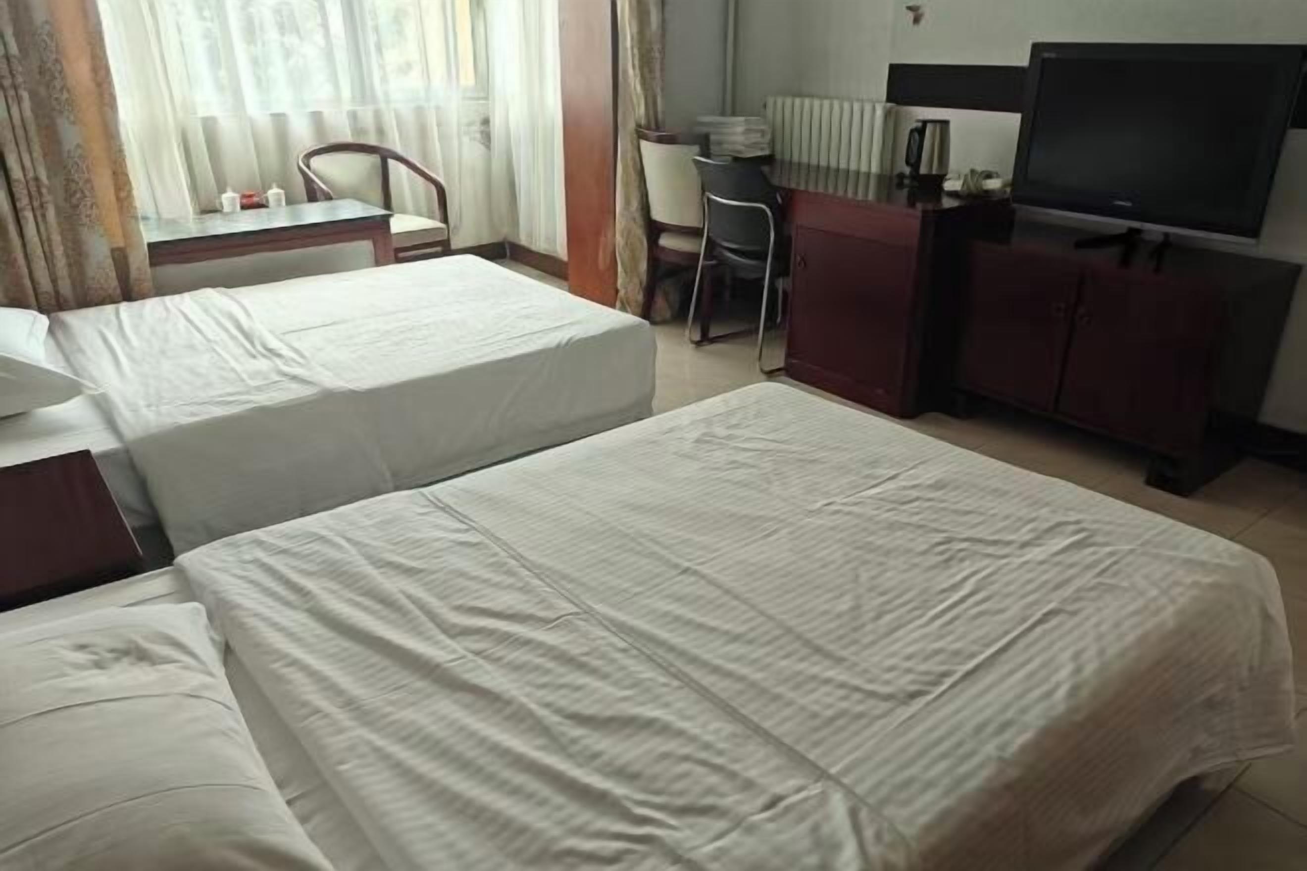 Habitación de hotel con dos camas, un escritorio, una silla, un televisor y un armario.