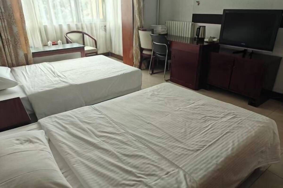 A hotel room with two beds, a desk, a chair, a TV, and a cabinet.