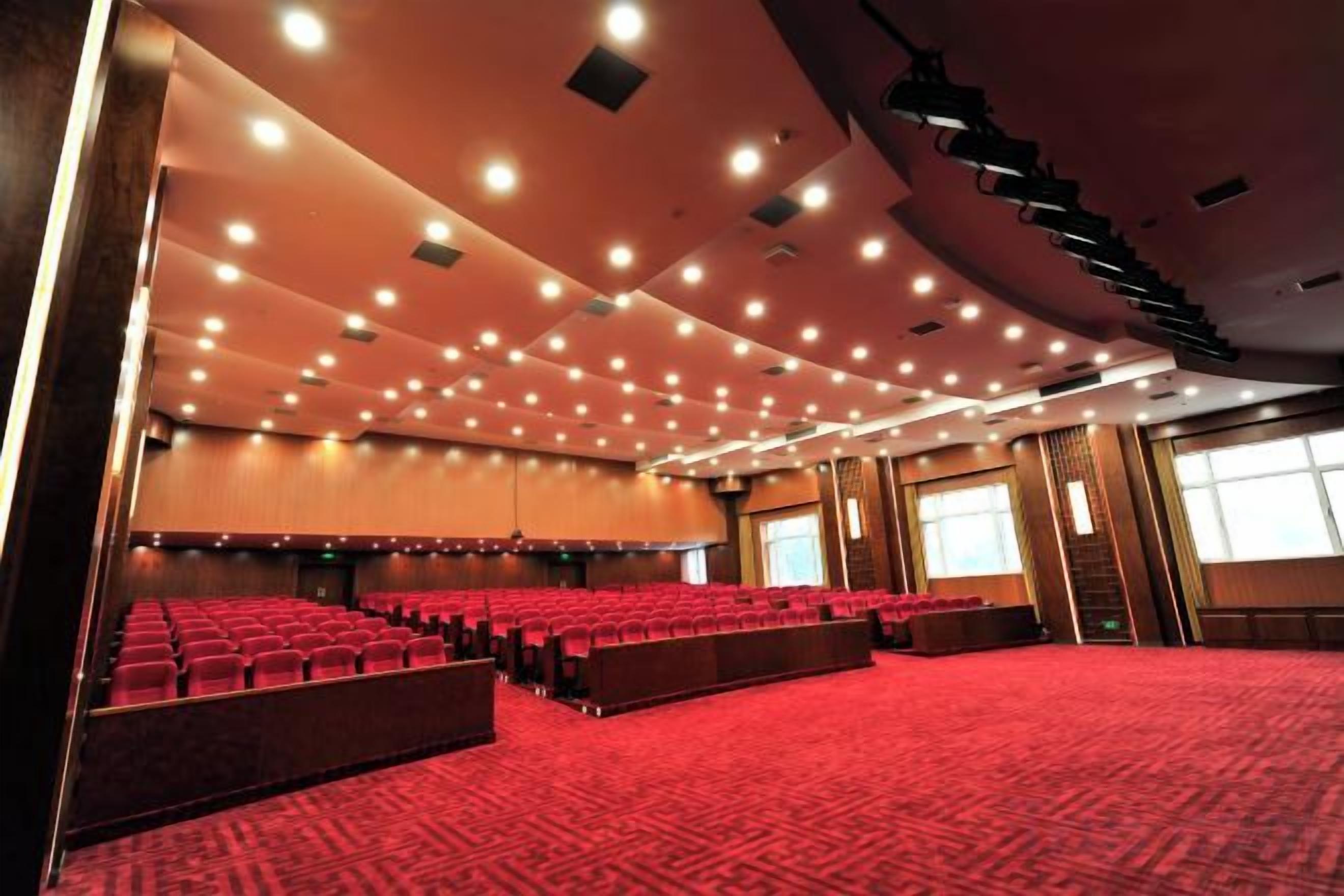 A large auditorium with rows of red seating, a carpeted floor, and a high ceiling with recessed lighting.