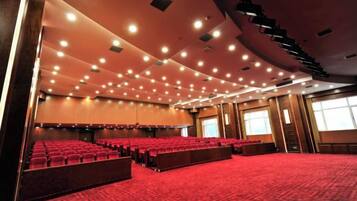 A large auditorium with rows of red seating, a carpeted floor, and a high ceiling with recessed lighting.